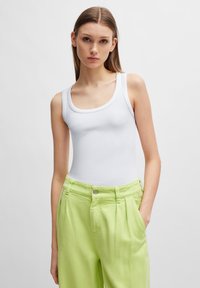 Hvit ribbet tanktopp med scoop hals er parret med lysegrønn, plissert bukse som har sidelommer og frontknapp-lukking.