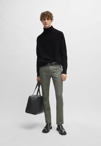 Zwarte coltrui, grijs patroon broek, zwarte riem, leren tas en zwarte schoenen. De look is op maat gemaakt met een moderne pasvorm.