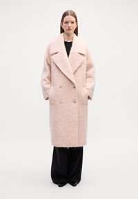 Casaco de double-breasted em rosa suave, feito de um tecido texturizado. Apresenta grandes lapelas, dois bolsos laterais e botões metálicos.