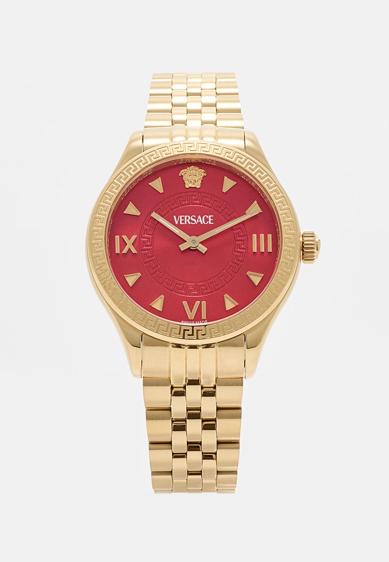 Reloj de tono dorado con esfera roja, marcadores en números romanos y el logo de Medusa. Presenta un bisel con patrón y una pulsera de eslabones de metal.