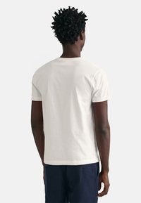 Hvid kortærmet bomulds t-shirt med rund halsudskæring. Glat tekstur, almindelig pasform. Uden funktioner på bagsiden, båret med marinefarvede bukser.