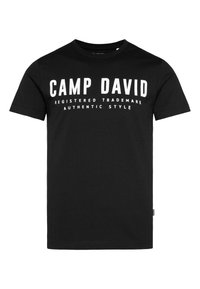 Camiseta de algodón negra con cuello redondo. Presenta un texto en blanco llamativo: “CAMP DAVID MARCA REGISTRADA ESTILO AUTÉNTICO” en la parte frontal.