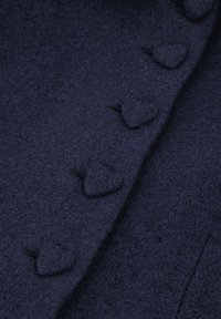 Casaco de lã azul-marinho com um acabamento texturizado, apresentando botões em forma de coração e um detalhe de costura vertical suave.