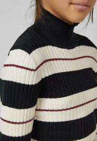 Zwart en roomkleurig ribgebreide coltrui met horizontale strepen, voorzien van dunne kastanjebruine accenten. Close-up toont textuur en ontwerp.