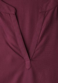 Encolure de chemise bordeaux profond avec un col en V et des détails de couture visibles sur une texture de tissu lisse.