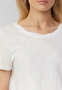 T-shirt blanc à manches courtes en tissu doux et léger, avec une apparence légèrement texturée et un col en V large.