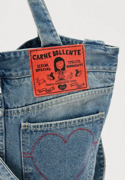 Džínový výrobok s červenou etiketou, na ktorej sú ilustrácie a text. Zadný vrecko je vyšívané s červeným srdiečkom.