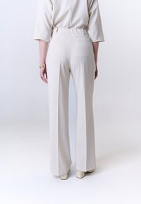 Beige hoge taille broek met een rechte snit, voorzien van een achterzak en een gladde textuur, gecombineerd met lichtgekleurde hakschoenen.