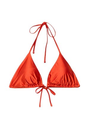 Žena v červenom bikini top a slnečných okuliaroch, ležiaca s vodnými kvapkami na pokožke na hnedom pozadí.