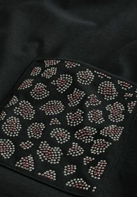 Tessuto nero con un patch testurizzato che presenta un design di stampa leopardata in strass argento e rosa, con una finitura liscia e bordi definiti.