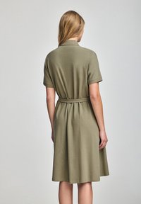Abito verde oliva a maniche corte con vita accentuata da una cintura, realizzato in tessuto morbido, con una silhouette semplice a trapezio e colletto.
