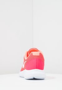 Bright coral and pink athletic shoe with white sole and white Nike swoosh viewed from the back on a white surface against a white background.