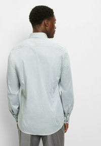 Hellblaues Hemd mit Knopfleiste, feinem geometrischem Muster, langen Ärmeln und klassischem Kragen, mit abgerundetem Saum und geknöpften Manschetten.