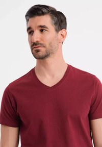 Vínová v-tričko vyrobené z bavlny, s krátkými rukávy a hladkým povrchem. Model se otáčí k objektivu na čistém pozadí.