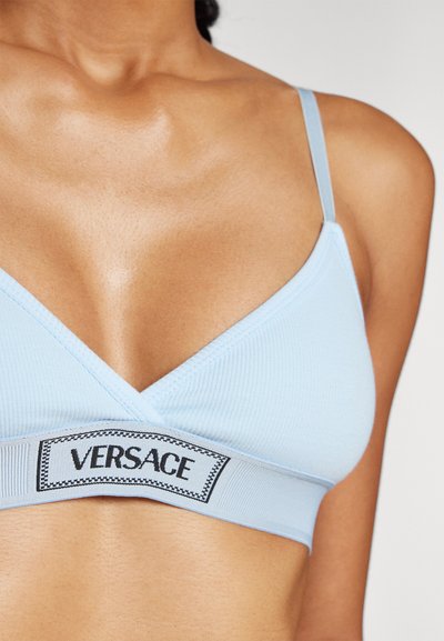 Gaiši zils bralets ar rievotu tekstūru, V-veida dekoltē, regulējamām siksnām un melnu "VERSACE" logo joslu apakšā.