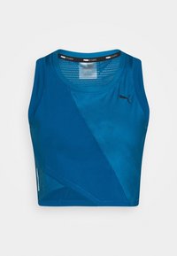 Modrý sportovní crop top z hladké, prodyšné tkaniny. Má kulatý výstřih, panelový design a černý logo akcent na přední straně.