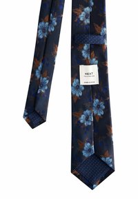 Jūras zila kaklasaite ar gaiši zilu un brūnu ziedu rakstu, ar uzrakstu "NEXT Tailoring Made in China".