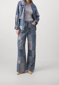 Denim jacket with a patchwork design and oversized fit, paired with wide-leg patchwork jeans in varying shades of blue, textured fabric.