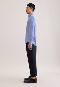 Jasnoniebieska, długorękawowa koszula o fakturowanym wzorze, zestawiona z ciemnoniebieskimi spodniami i czarnymi butami. Widoczne detale guzików na koszuli.