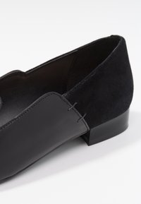 Svarta loafers med läderöverdel, mockadetaljer, en slät yta och en låg blockklack; minimal sömnadsdetalj synlig.