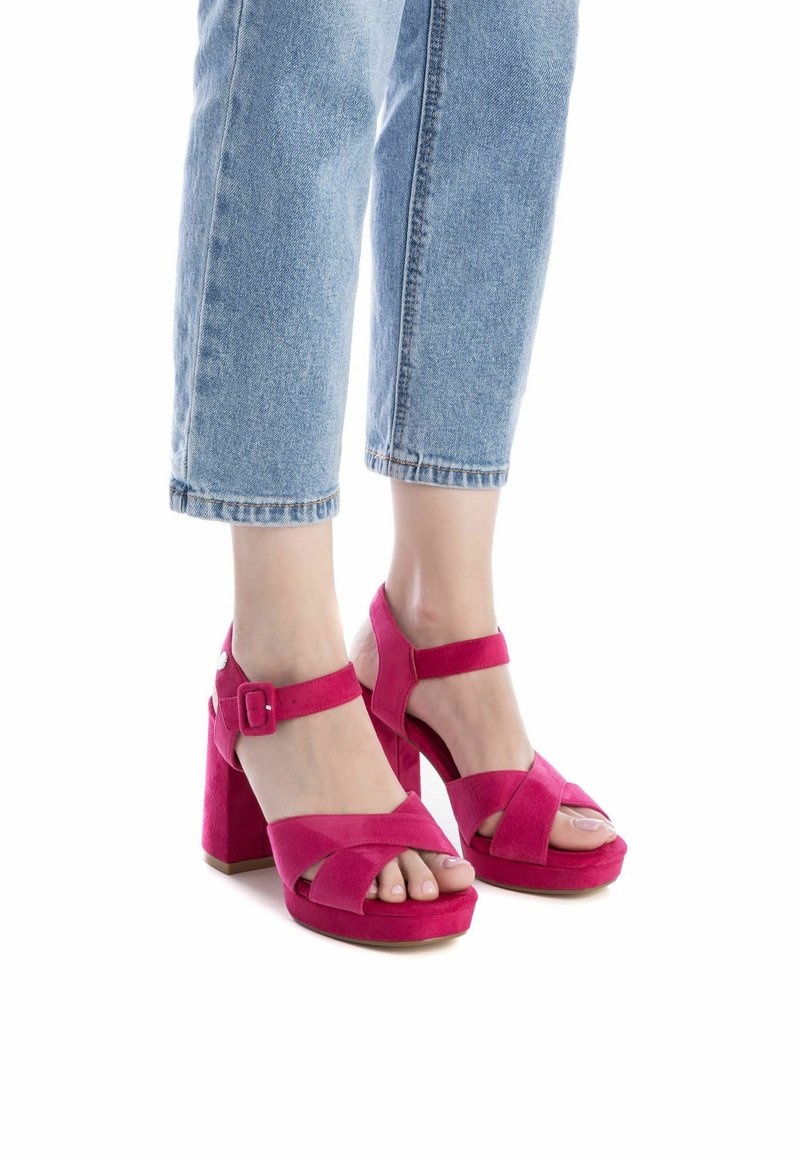 Zapatos de tacón de plataforma de ante rosa con diseño de tiras cruzadas y hebilla en el tobillo, con un tacón cuadrado alto y puntera abierta. Pantalones de mezclilla cortos visibles.