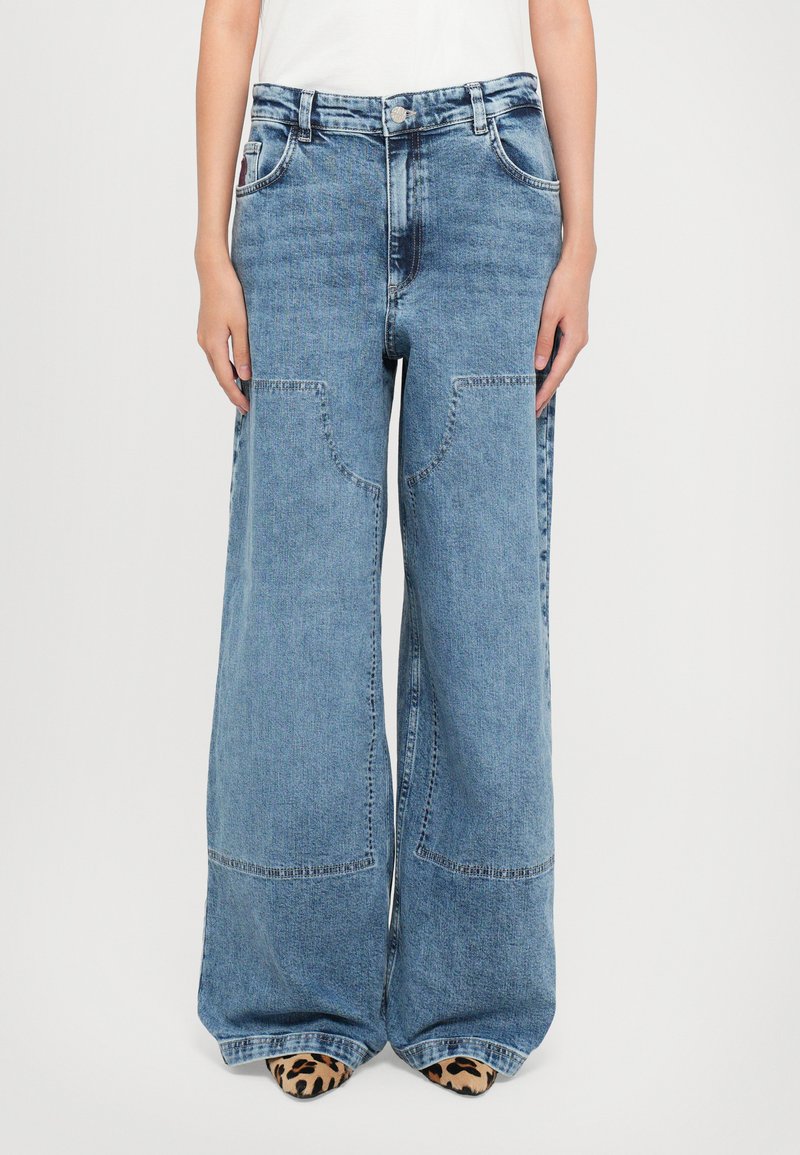 Wide-leg denim jeans in light blue, featuring large patch pockets, contrasting stitching, and a high-waisted design.