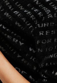 Czarny pluszowy koc z srebrnym tekstem na całej powierzchni. Tkanina ma miękką, puszystą strukturę z powtarzającym się wzorem słów.