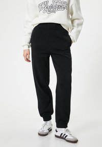 Schwarze Sweatpants mit einer lockeren Passform, elastischem Bund und gerippten Bündchen, kombiniert mit einem weißen Sweatshirt, das ein schwarzes Textdesign aufweist.