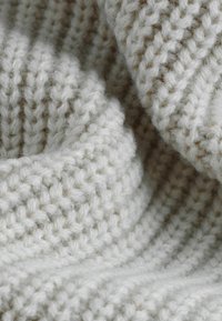 Gros plan sur un tissu en laine tricotée épaisse, douce et blanc cassé, avec un motif côtelé et une texture ainsi que des fibres visibles.