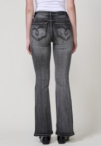 Jeans acampanados en denim gris oscuro, con una cintura de altura media, costuras distintivas en los bolsillos traseros y una textura suave con mínimas abrasiones.
