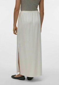 Jupe maxi blanche avec une taille élastique froncée et une fente sur le côté. Le tissu a une texture lisse et légère. Associée avec des ballerines noires.