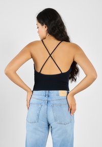 Svart smocket tanktop med tynne kryssede stropper, kombinert med lyseblå høyt midje denimjeans med firkantet baklapp og lommer.