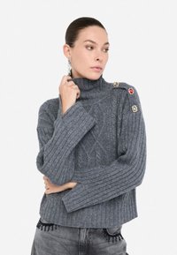 Maglione grigio corto con collo a imbuto, caratterizzato da una texture a costine e bottoni decorativi rossi e dorati sulla spalla.