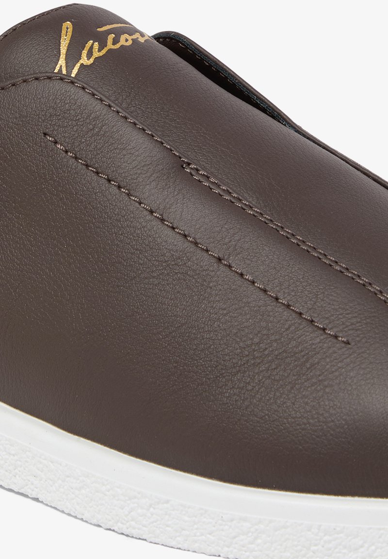 Scarpa slip-on in pelle marrone scuro con cuciture centrali a vista e suola bianca texture, con logo dorato in corsivo vicino all'apertura.