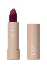 Rouge à lèvres ILIA dans un tube beige avec une marque blanche ; présente un bâton riche bordeaux. Texture lisse et forme classique.