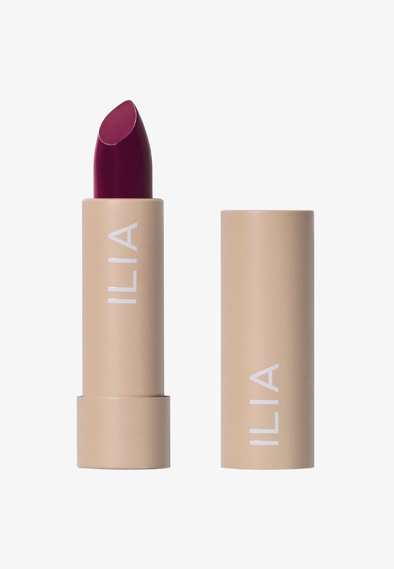 ILIA läppstift i ett beige rör med vit branding; har en fyllig burgundy-färg på stiftet. Slät textur och klassisk bullet-form.