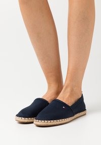 Espadrillas in tela blu navy con suola in corda di juta, caratterizzate da una punta rotonda e dettagli cuciti lungo la suola. Accento di branding minimale.