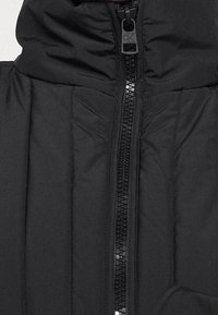 Chaqueta acolchada negra con cierre frontal, costuras verticales para textura y un diseño de cuello alto. El material parece suave y aislante.