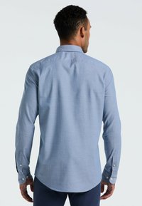 Blaue Hemdbluse mit langen Ärmeln, strukturiertem Stoff und abgerundetem Saum. Verfügt über Knopfmanschetten und einen klassischen Kragen.