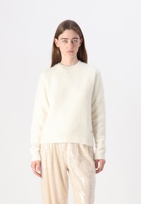 Maglione crema a trama con scollo rotondo e orlo a costine, abbinato a pantaloni beige larghi con paillettes e cintura elastica.