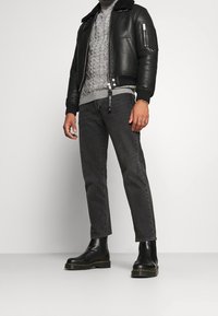 Veste aviateur en cuir noir avec col en shearling, pull gris à torsades, jeans gris foncé et bottines Chelsea noires à semelle texturée.