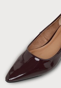 Chaussure plate brillante marron foncé à bout pointu avec doublure intérieure beige rembourrée sur fond clair.