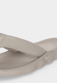 Ανοιχτό μπεζ σανδάλι Nike slide με φαρδιά λωρίδα και υφασμένη σόλα, με μικρό λογότυπο Nike swoosh στο πλάι.