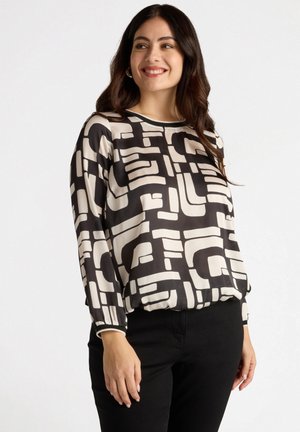 Blusa en blanco y negro con un patrón geométrico, mangas largas y cuello redondo. La tela parece suave y ligera.