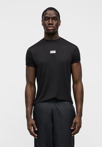 Μαύρο κοντομάνικο μπλουζάκι από λείο ύφασμα, με μικρό σήμα EA7 στο στήθος. Σετ με σκούρα σορτς με καρό σχέδιο.