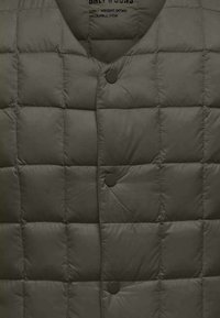Gilet en duvet léger de couleur vert olive foncé, avec un motif matelassé, un col arrondi et une fermeture à boutons-pression. Design compressible.