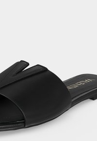 Sandale plate en cuir noir avec bout ouvert et large bride décorée d'un design en relief "V", semelle rembourrée et petit talon.