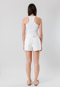 Canotta bianca a coste con un design aderente, abbinata a pantaloni shorts di jeans bianchi a vita alta con orli sfrangiati e due tasche posteriori.