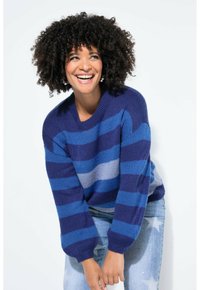 Maglione lavorato a maglia con righe verticali blu e navy, scollo rotondo e maniche larghe, abbinato a jeans azzurri slavati e strappati.