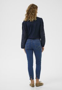 Laivaston sininen pusero, jossa on pitsiset puffihihat, yhdistettynä istuviin sinisiin farkkuihin, joissa on rusettiyksityiskohtia helmoissa ja kaksi takataskua ompelutiedoilla.